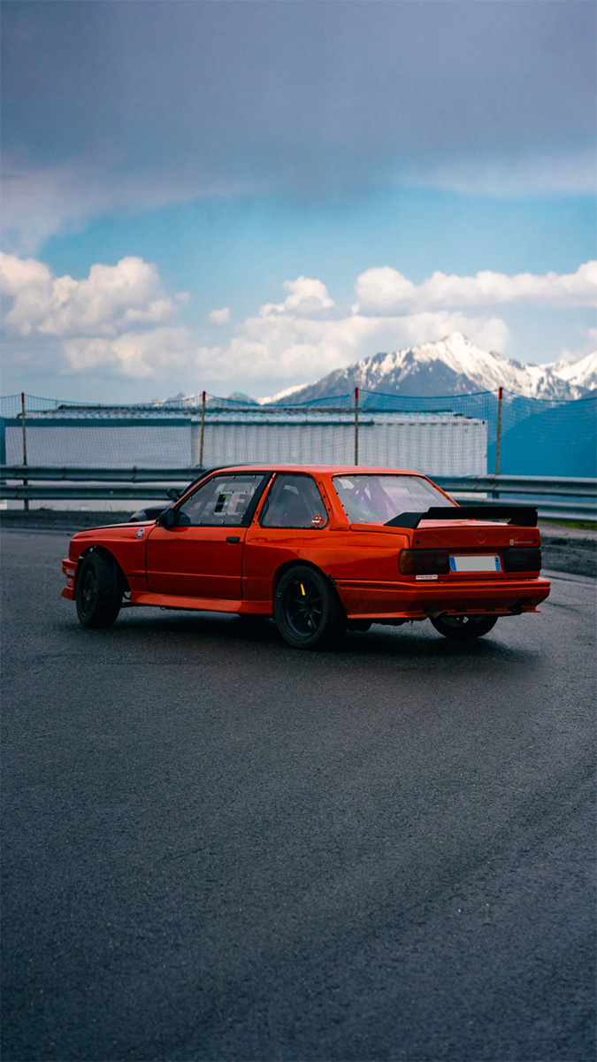 Photo d'une BMW e30 orange en train de drifter avec des montagnes en arriere plan