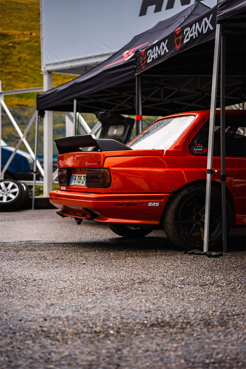 Photo d'une BMW e30 orange sous une pergola au circuit d'Andorre
