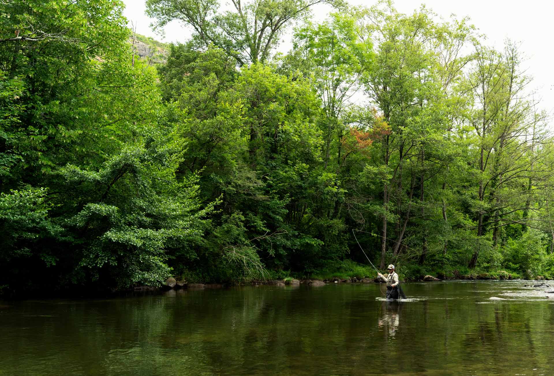 Pêcheur à la mouche, les pieds dans l'eau, en train de charger sa soie